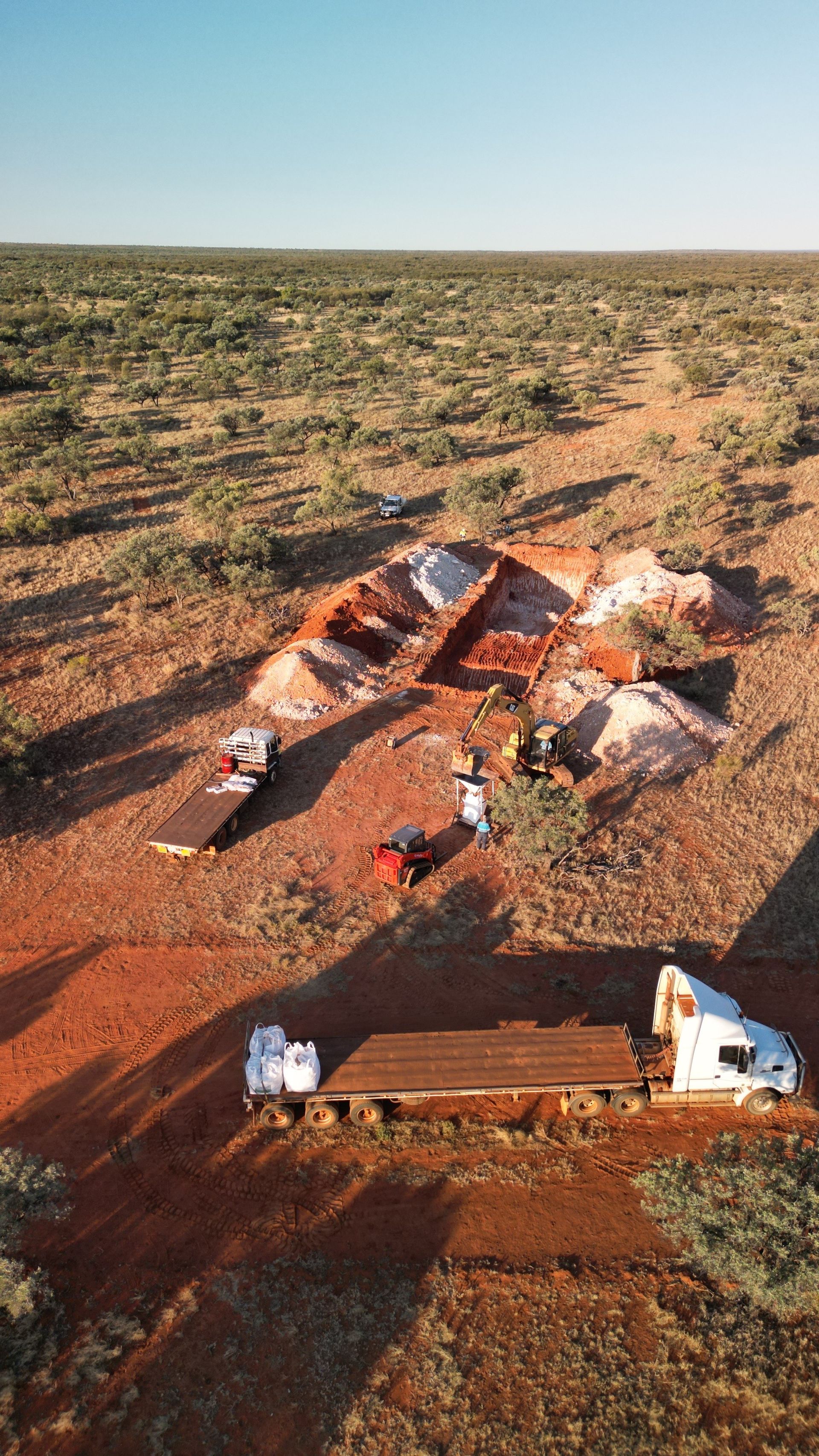 Trucks, soil piles, and people in a desert-like setting under a clear sky.