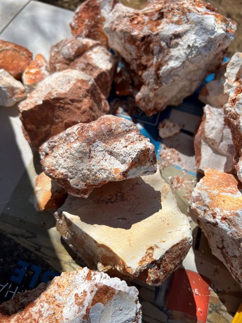 Pile of reddish-brown rocks with white patches on a light surface. Some rocks are in shadow.