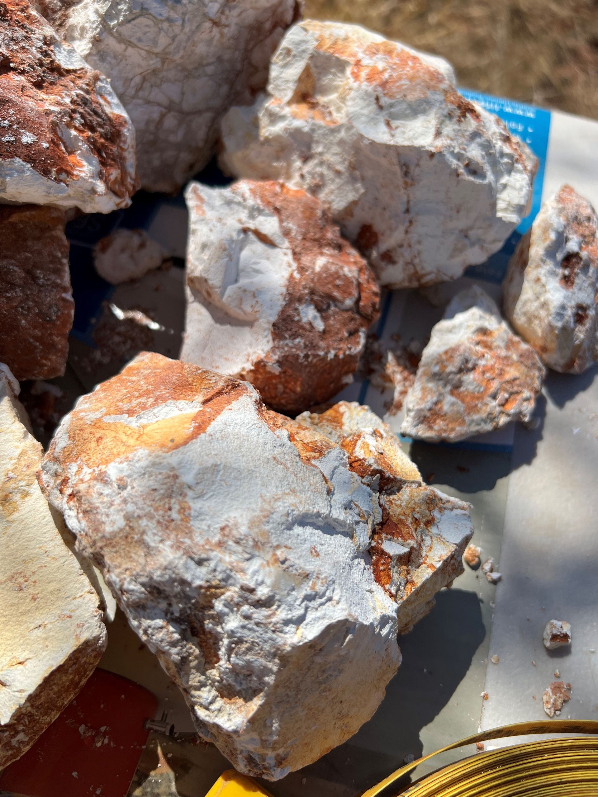 White and orange-red rocks, possibly ore, piled outdoors on a light-blue surface.