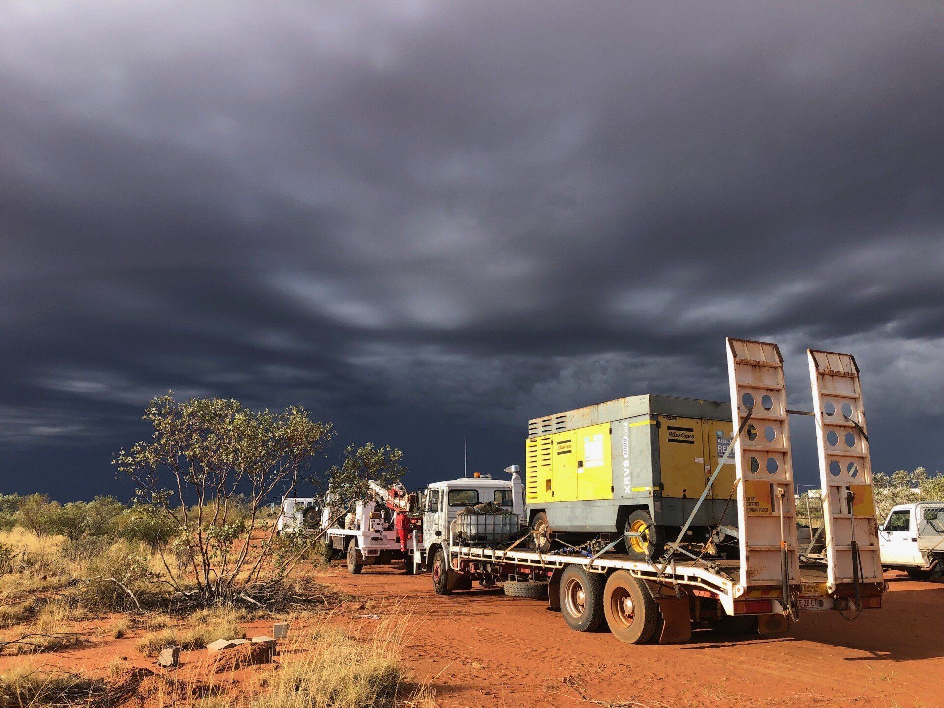 Truck carrying equipment on red dirt road under stormy sky.