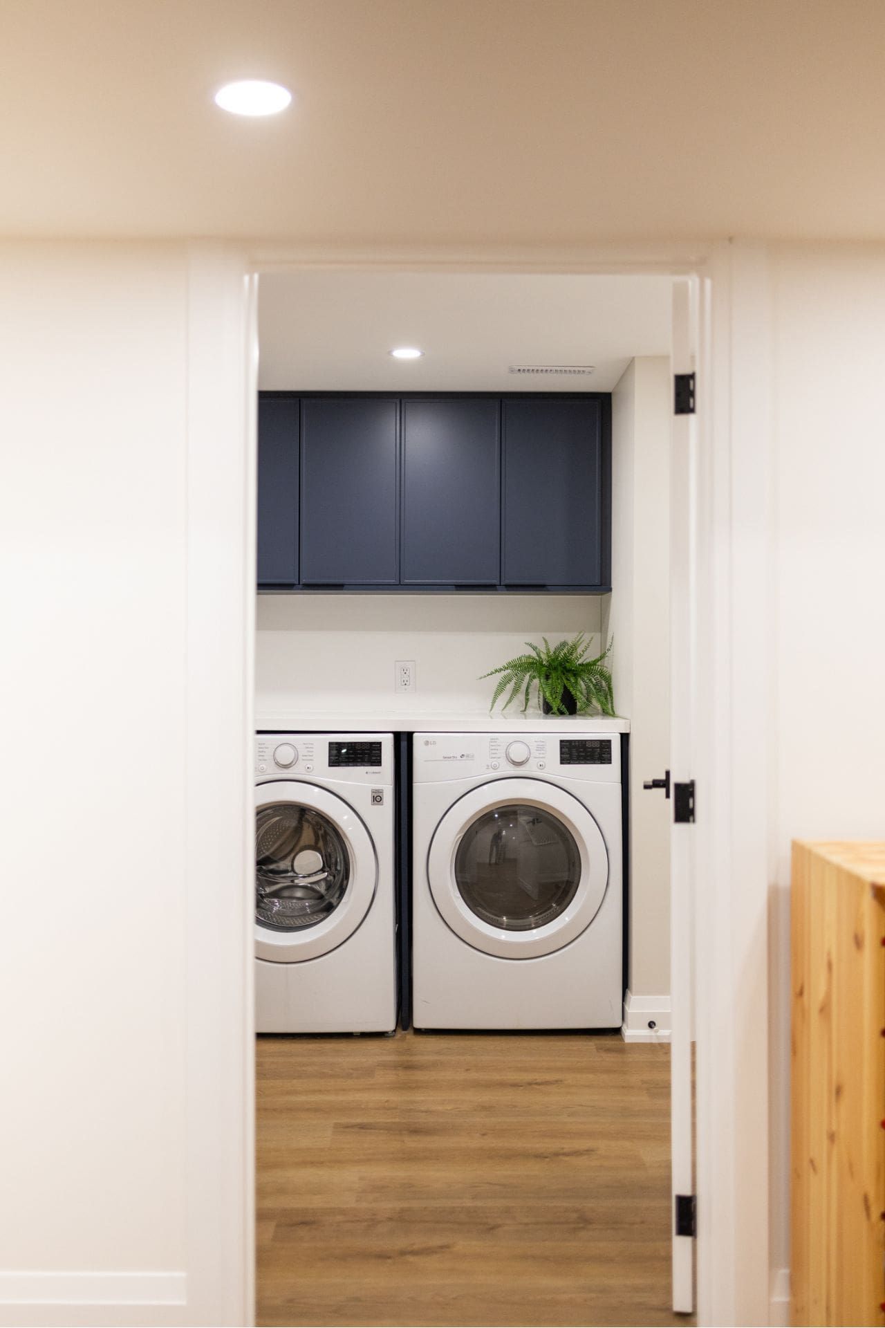 Laundry room with white appliances, navy cabinets, and wooden floor visible through an open doorway.