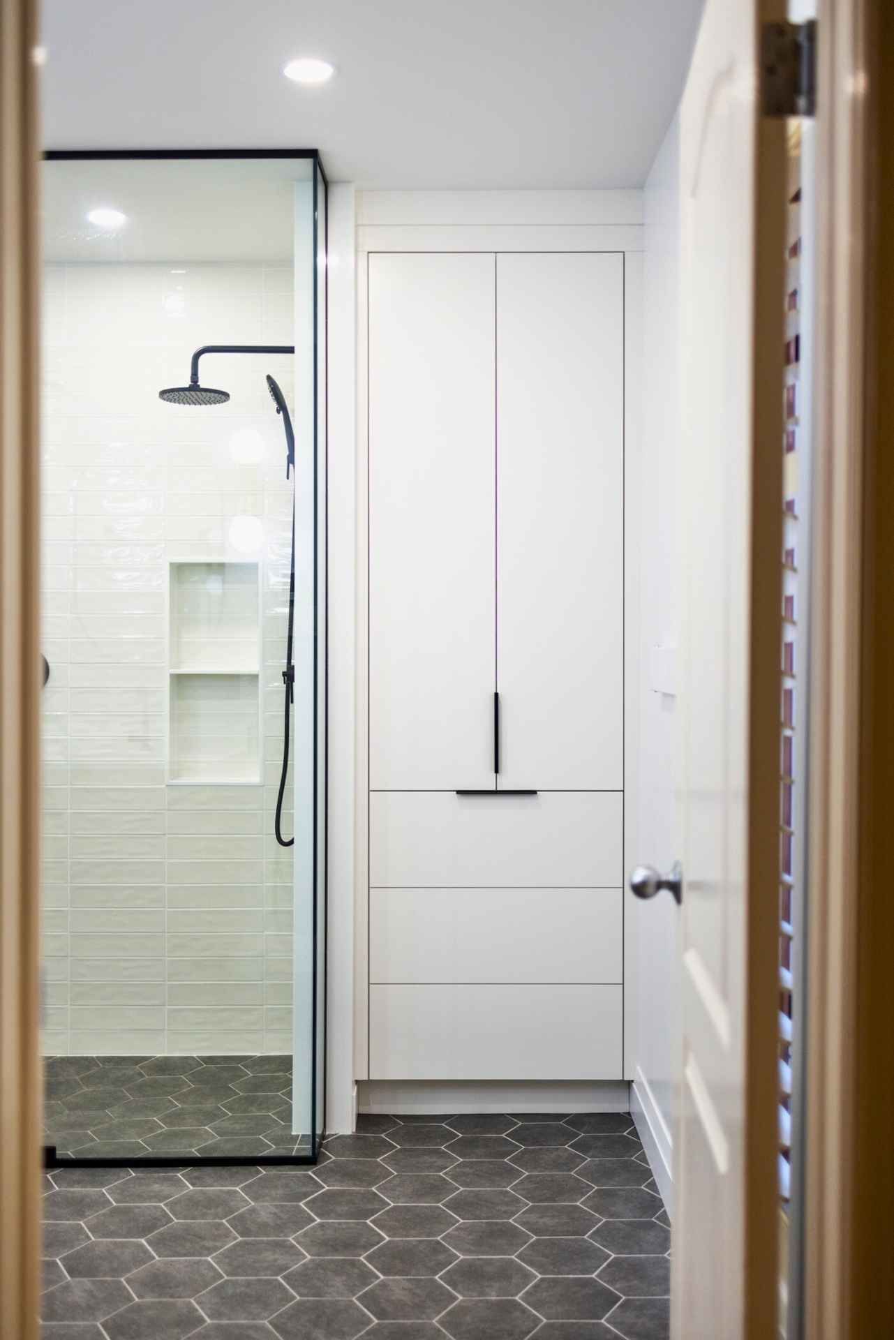 Bathroom with a glass-enclosed shower, white cabinet, and gray hexagon tile floor.