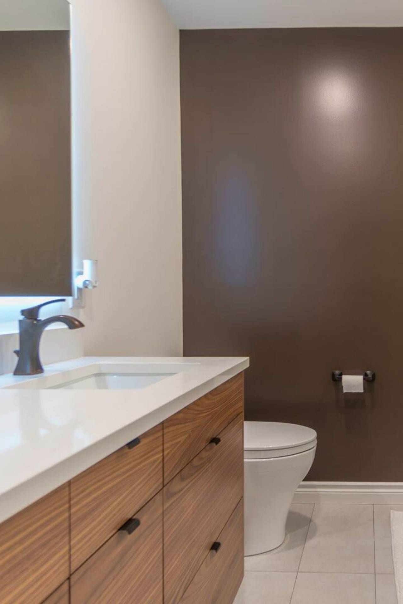 Modern bathroom with brown accent wall, wooden vanity, white countertop, and toilet.