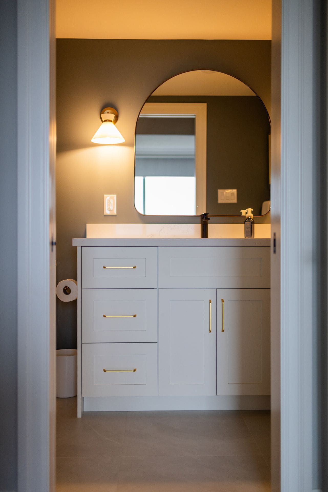 Bathroom interior with white vanity, arched mirror, and brass fixtures.