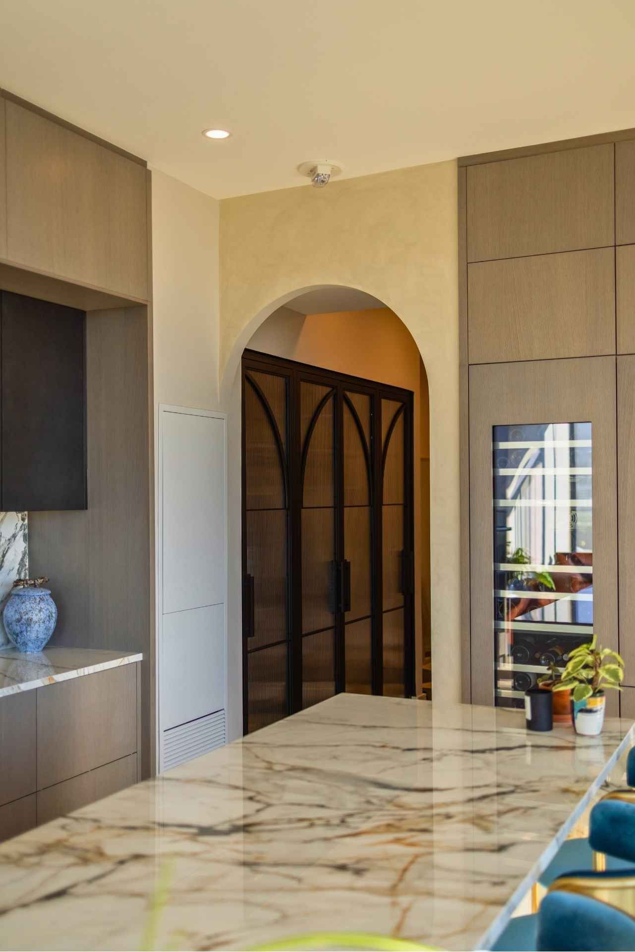 Kitchen with arched doorway, marble countertop, wine fridge, and black metal doors.