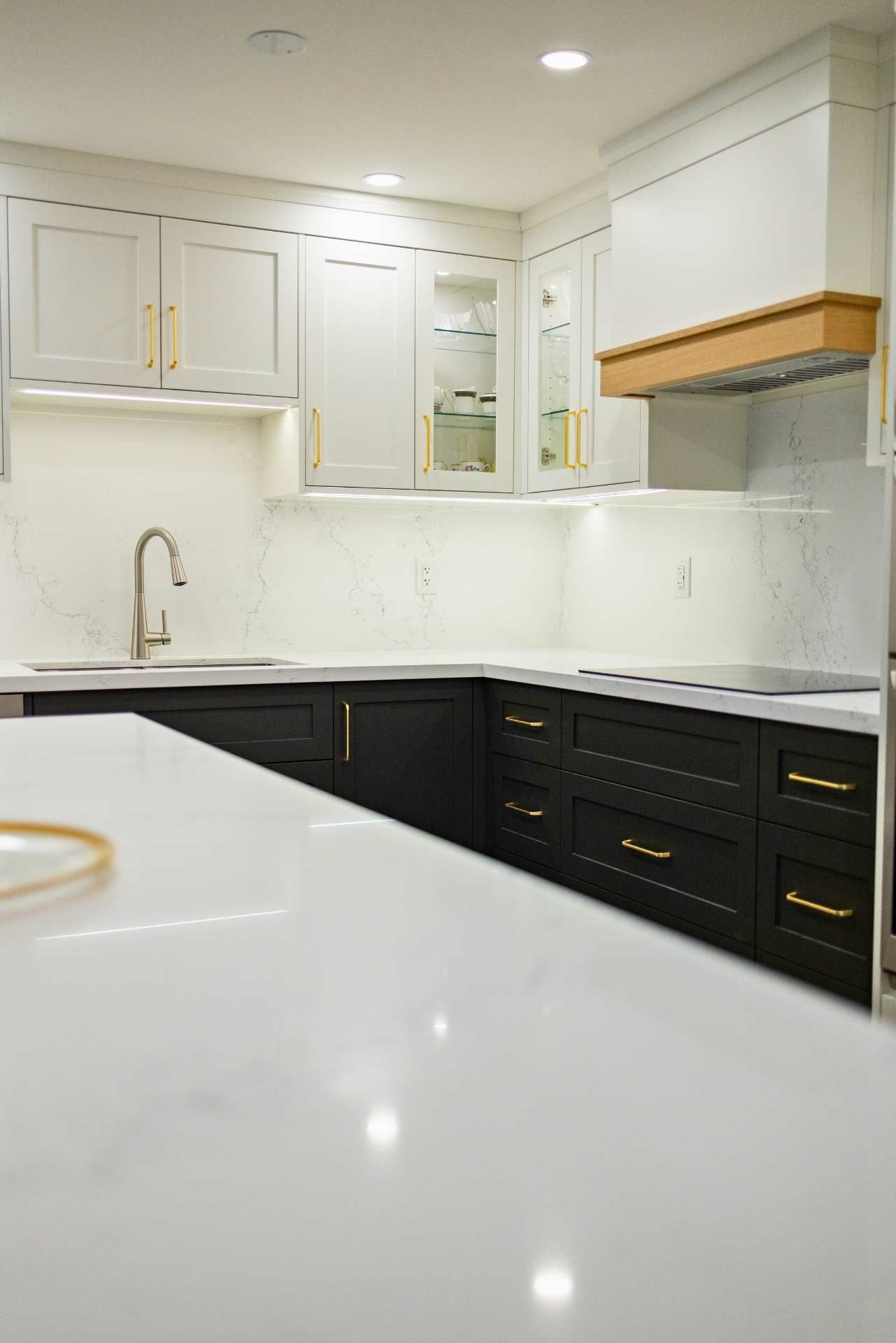 Modern kitchen with white and black cabinets, gold hardware, and a large white countertop.