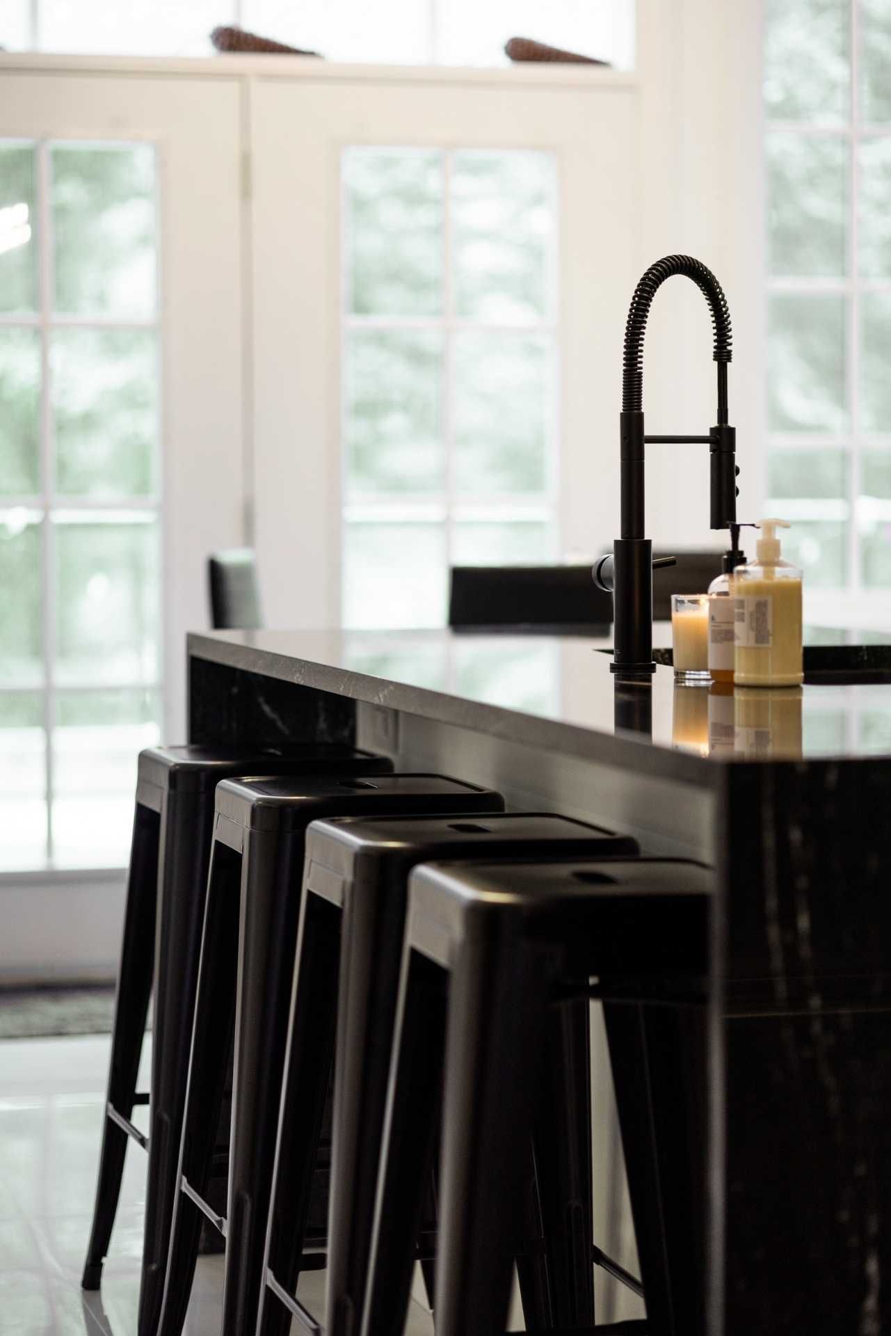 Black kitchen island with stools, faucet, and soaps in front of a window.