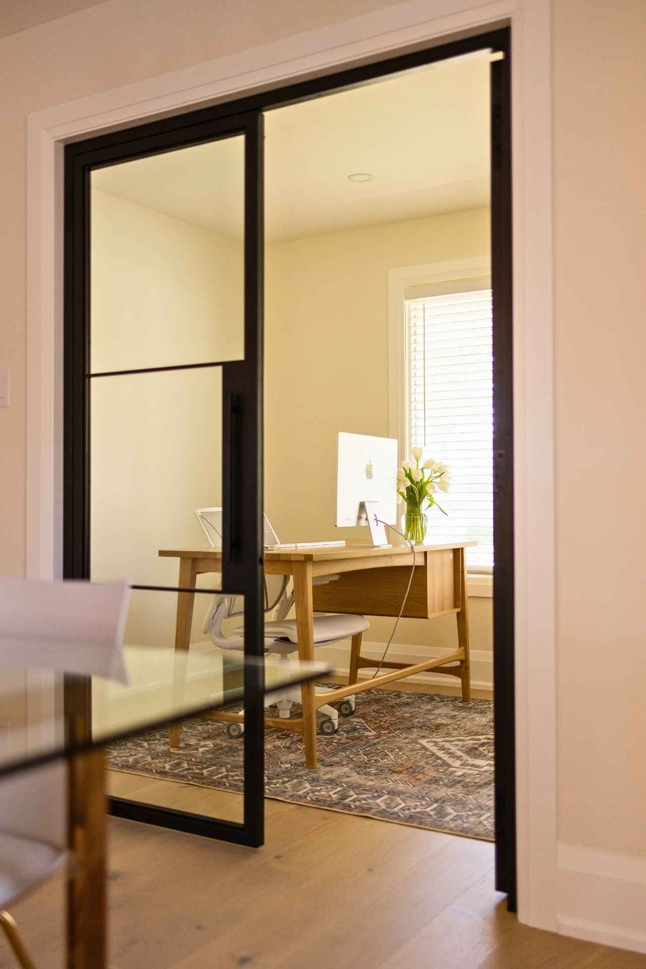 Black-framed glass sliding door leading to an office with a desk, chair, and computer.