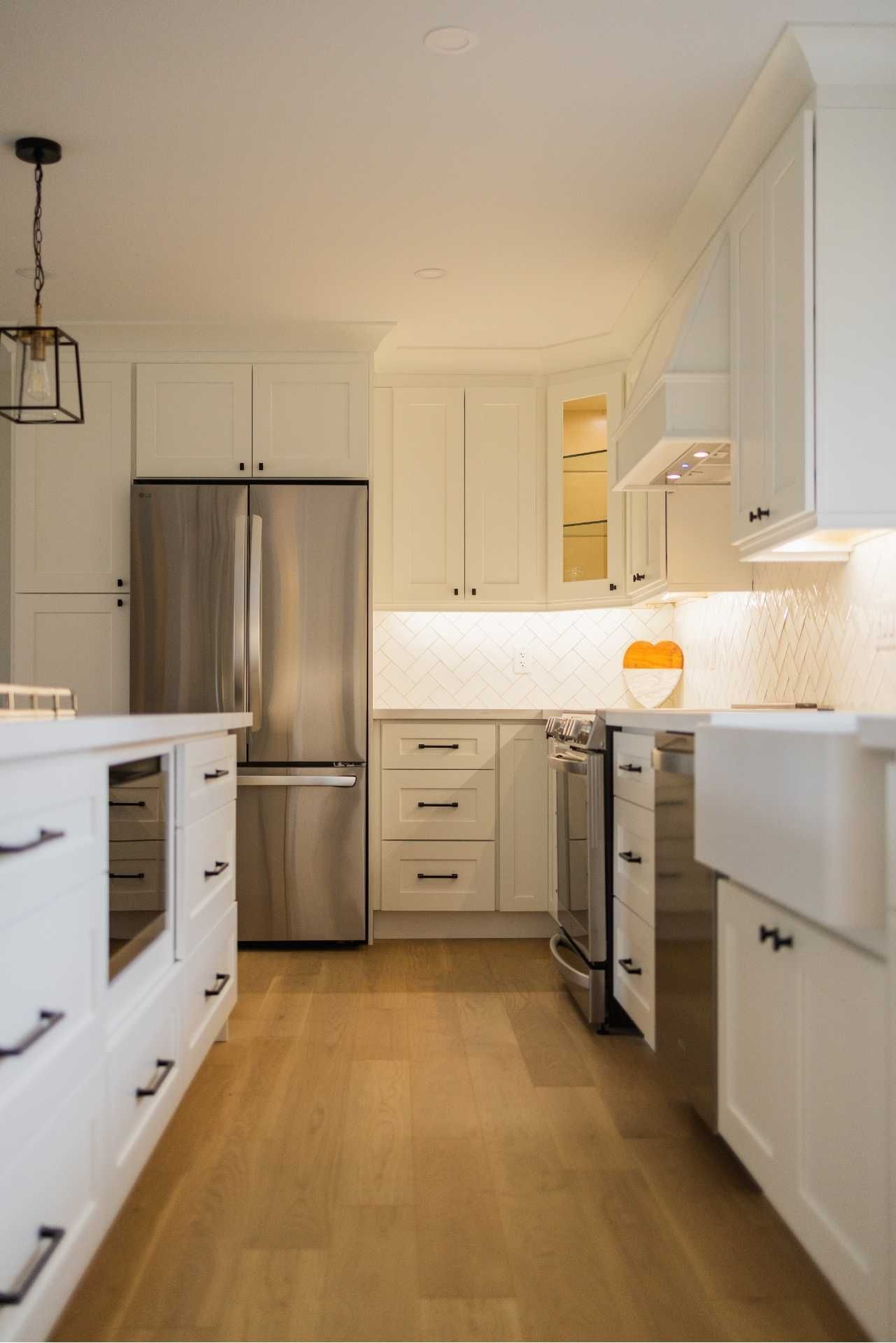 White kitchen with stainless steel appliances, island, and light wood floors.