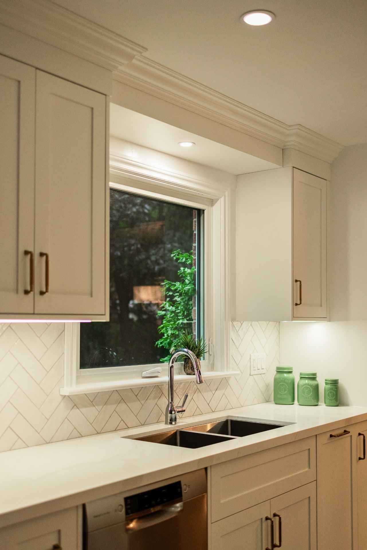 White kitchen with sink, cabinets, window overlooking greenery, and light fixtures.