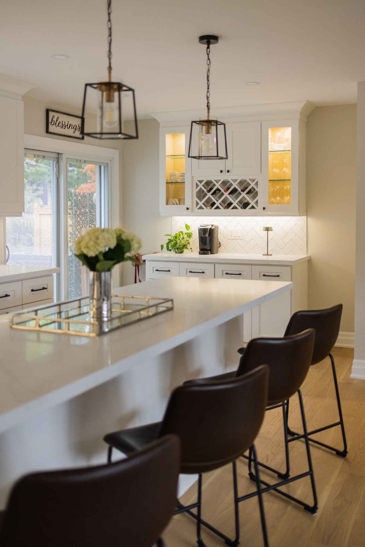 Modern kitchen with white cabinets, marble countertops, bar stools, and pendant lights.