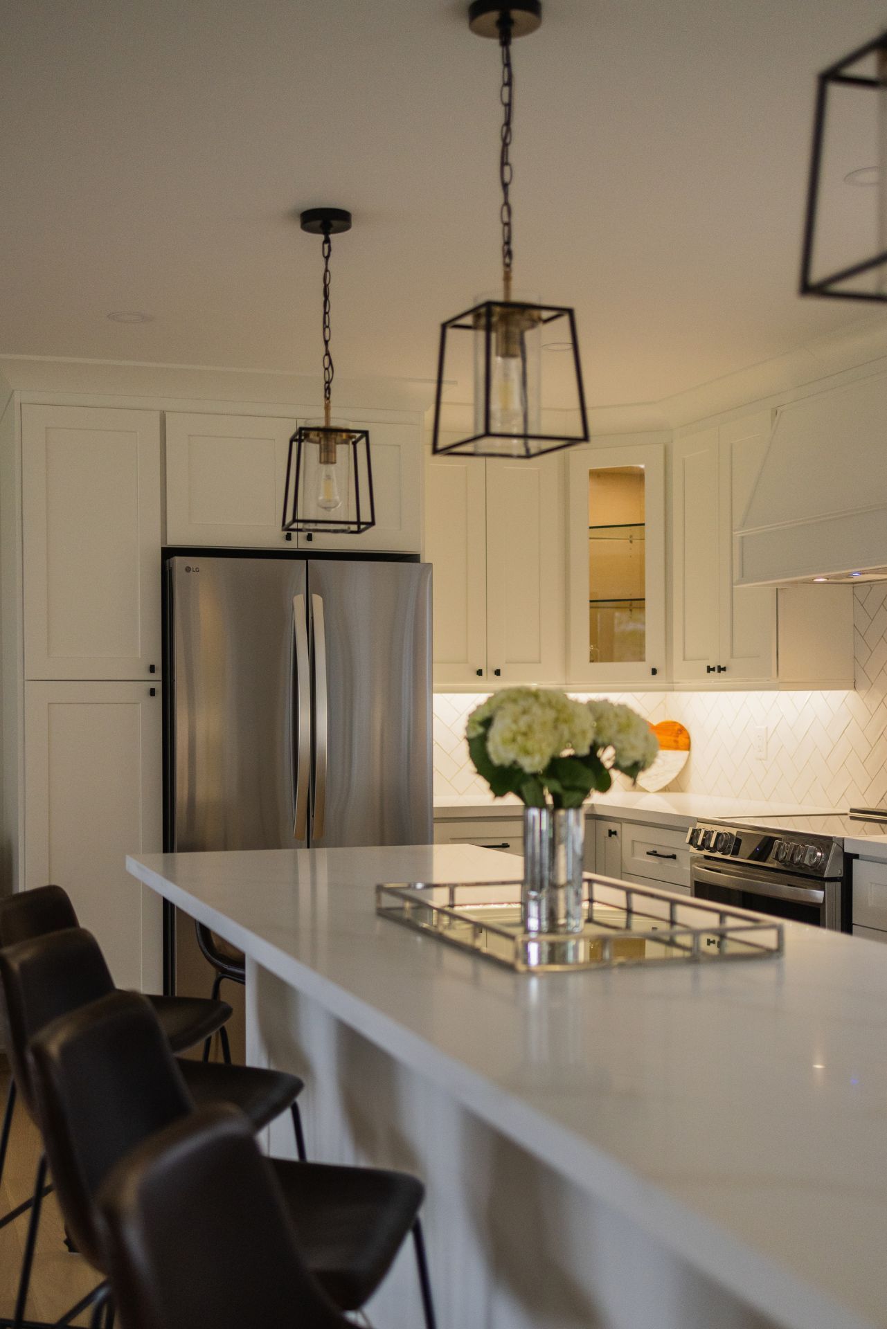 Kitchen with white cabinets, stainless steel refrigerator, island with seating, and pendant lights.