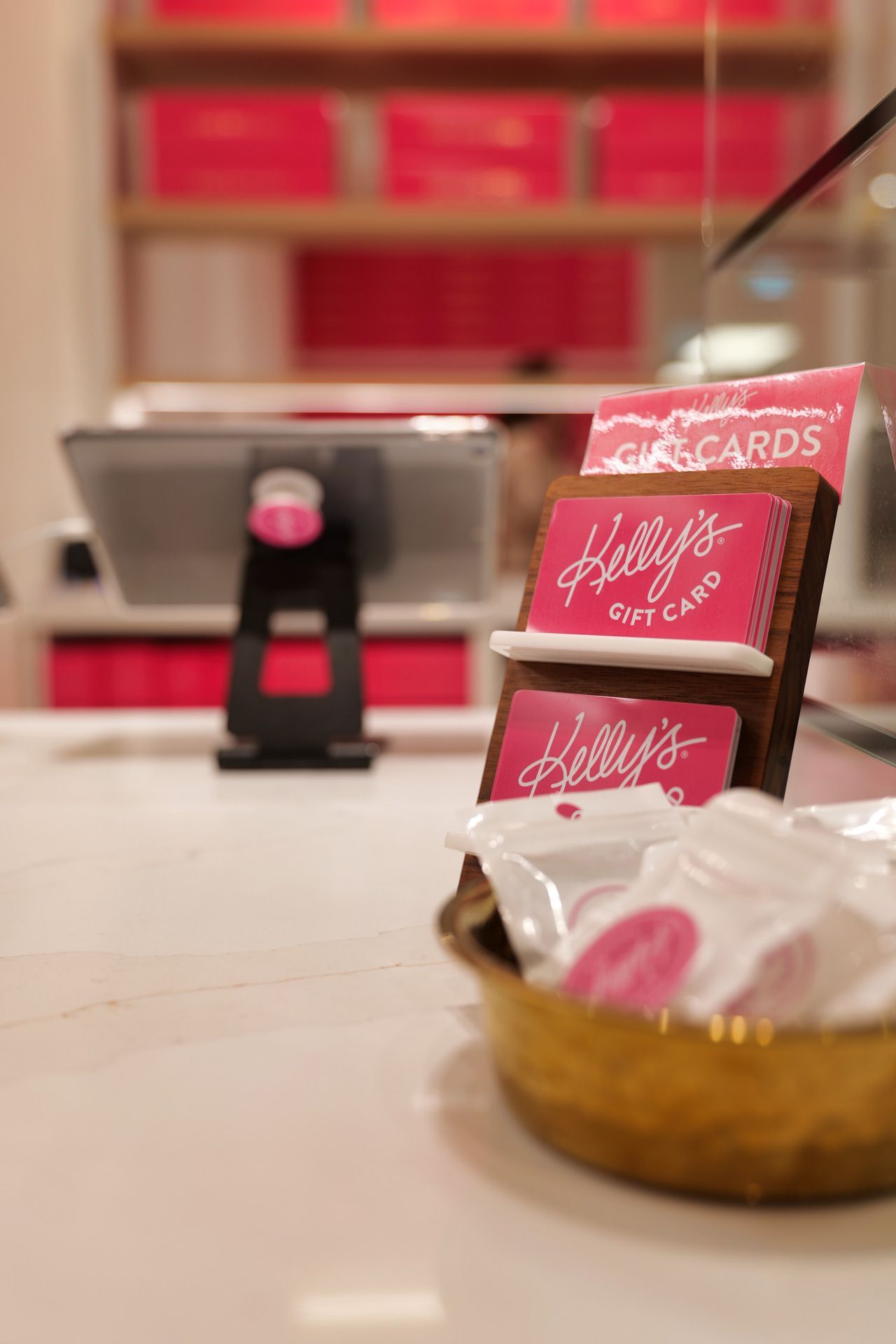 A counter with gift cards, a tablet, and treats in a shop with pink branding.