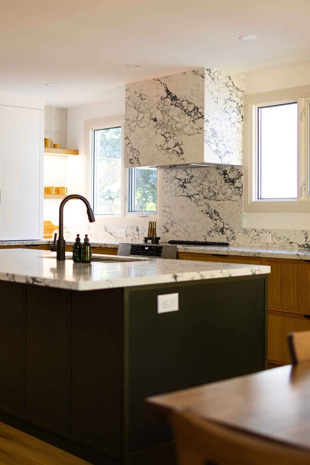 Modern kitchen with marble range hood, island with faucet, and windows.