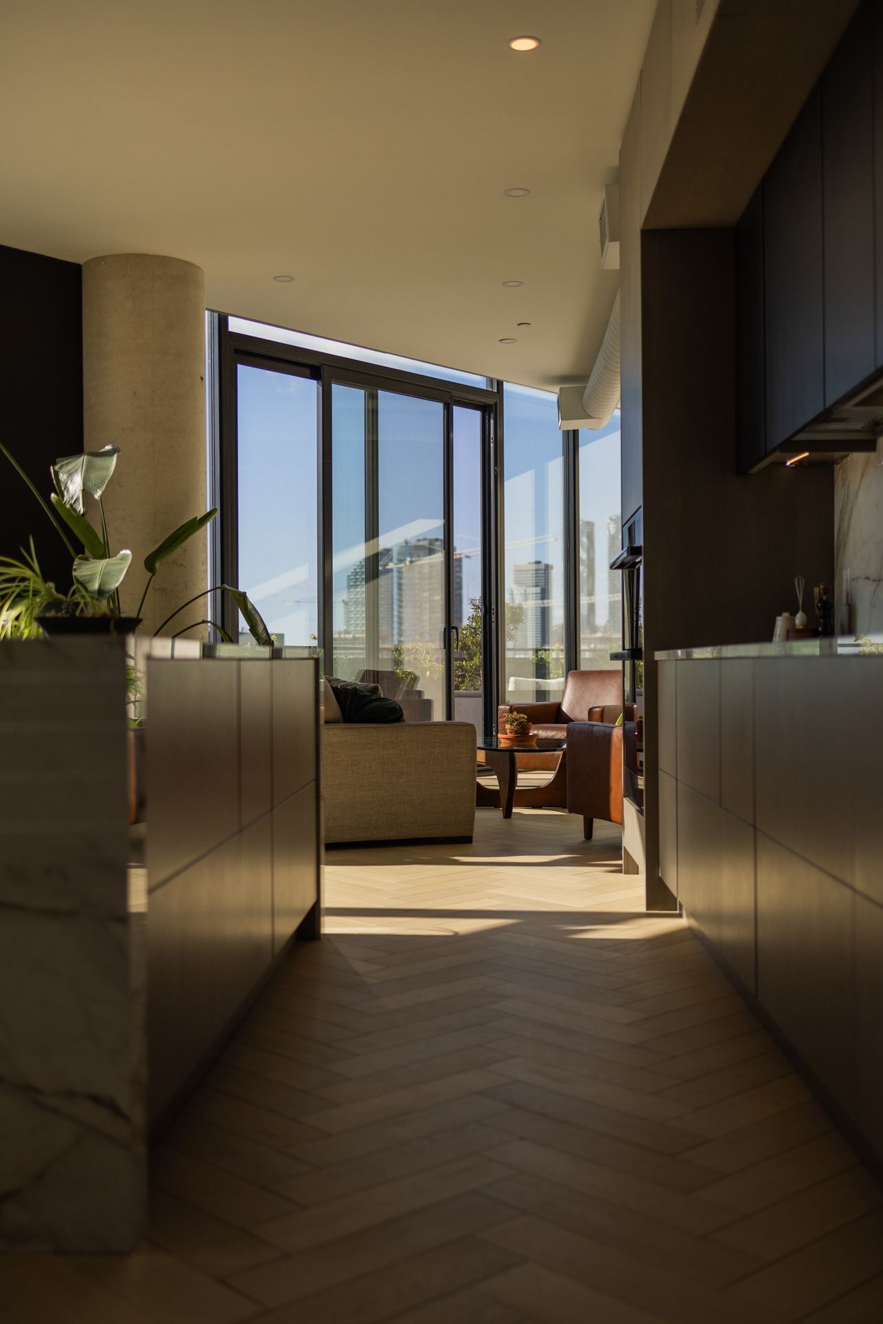 Modern kitchen with light wood floor, tall windows, and city view.