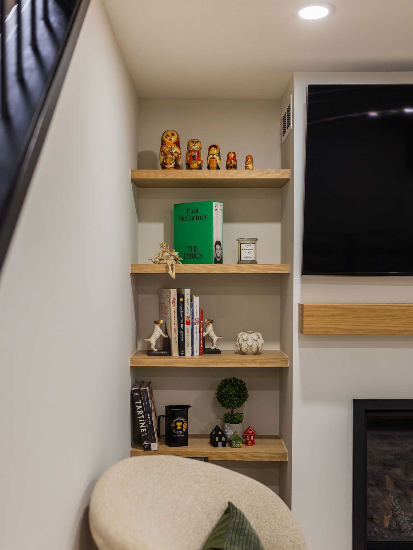 Built-in shelving with wooden shelves. Displays include books, figurines, and nesting dolls. Next to a fireplace and chair.