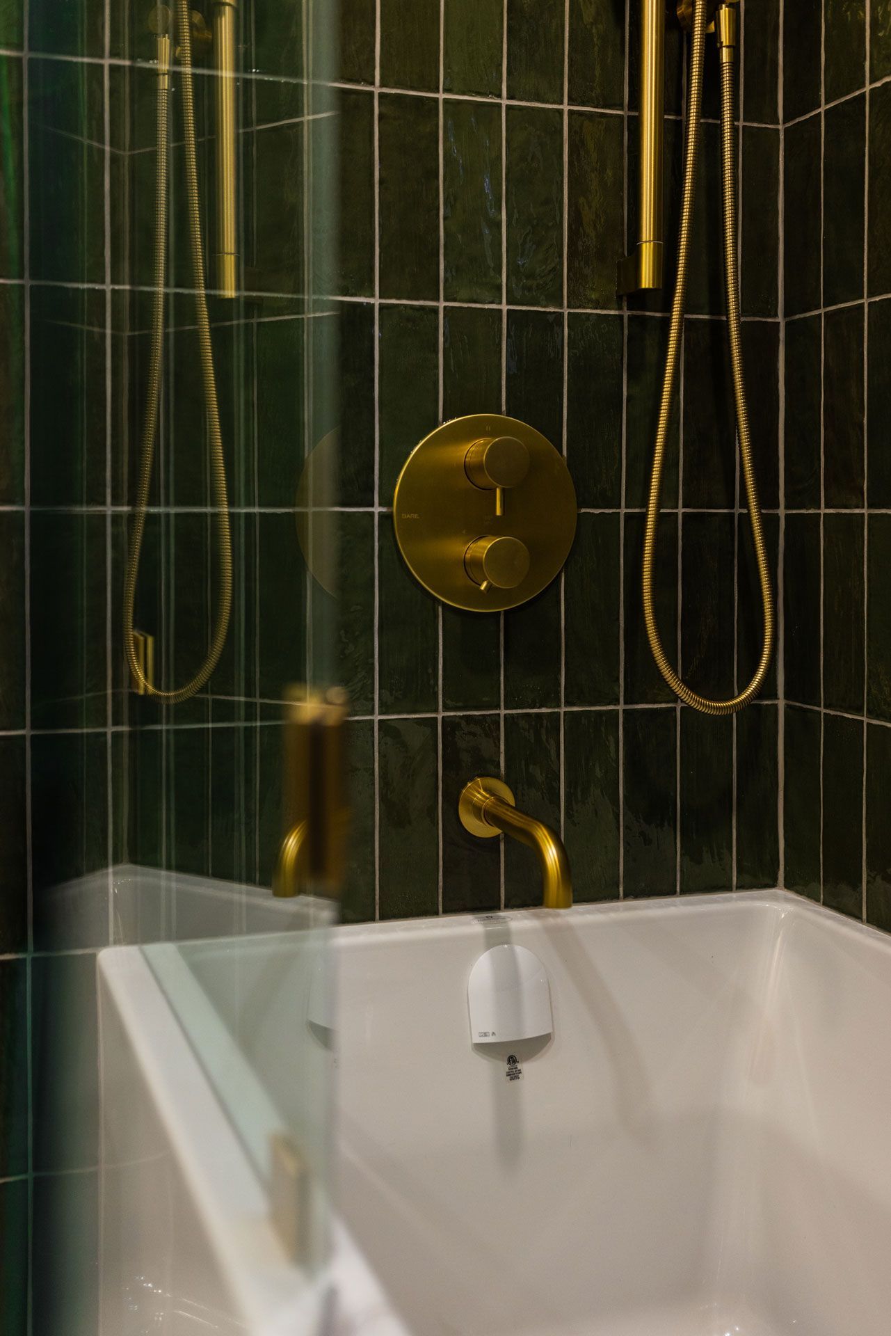 Gold shower fixtures against dark green tile in a bathroom. White bathtub visible.
