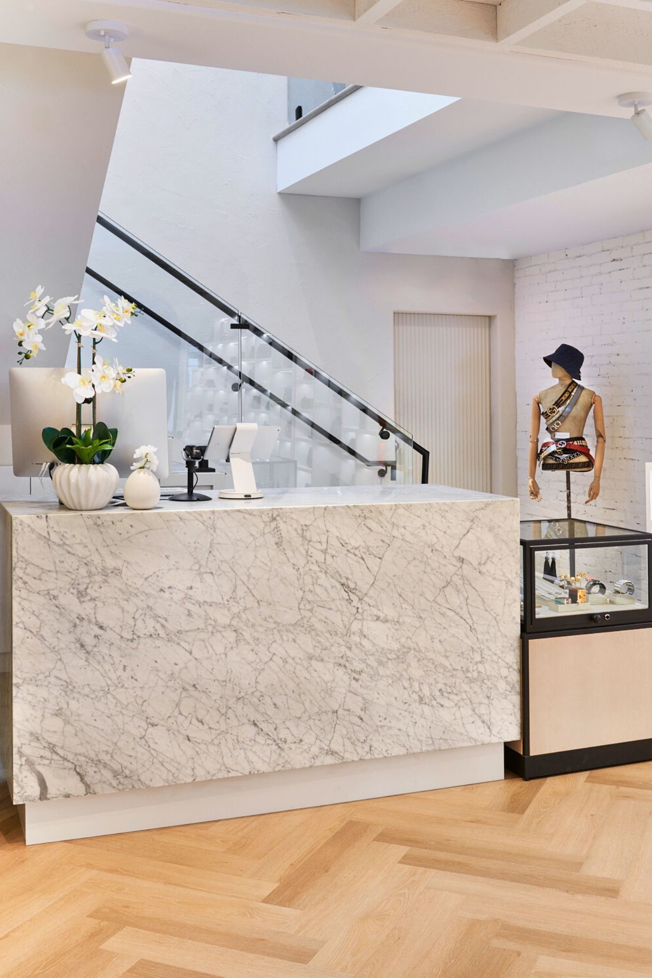 Marble reception desk in a bright, modern store, stairs leading upward, mannequin display in the background.