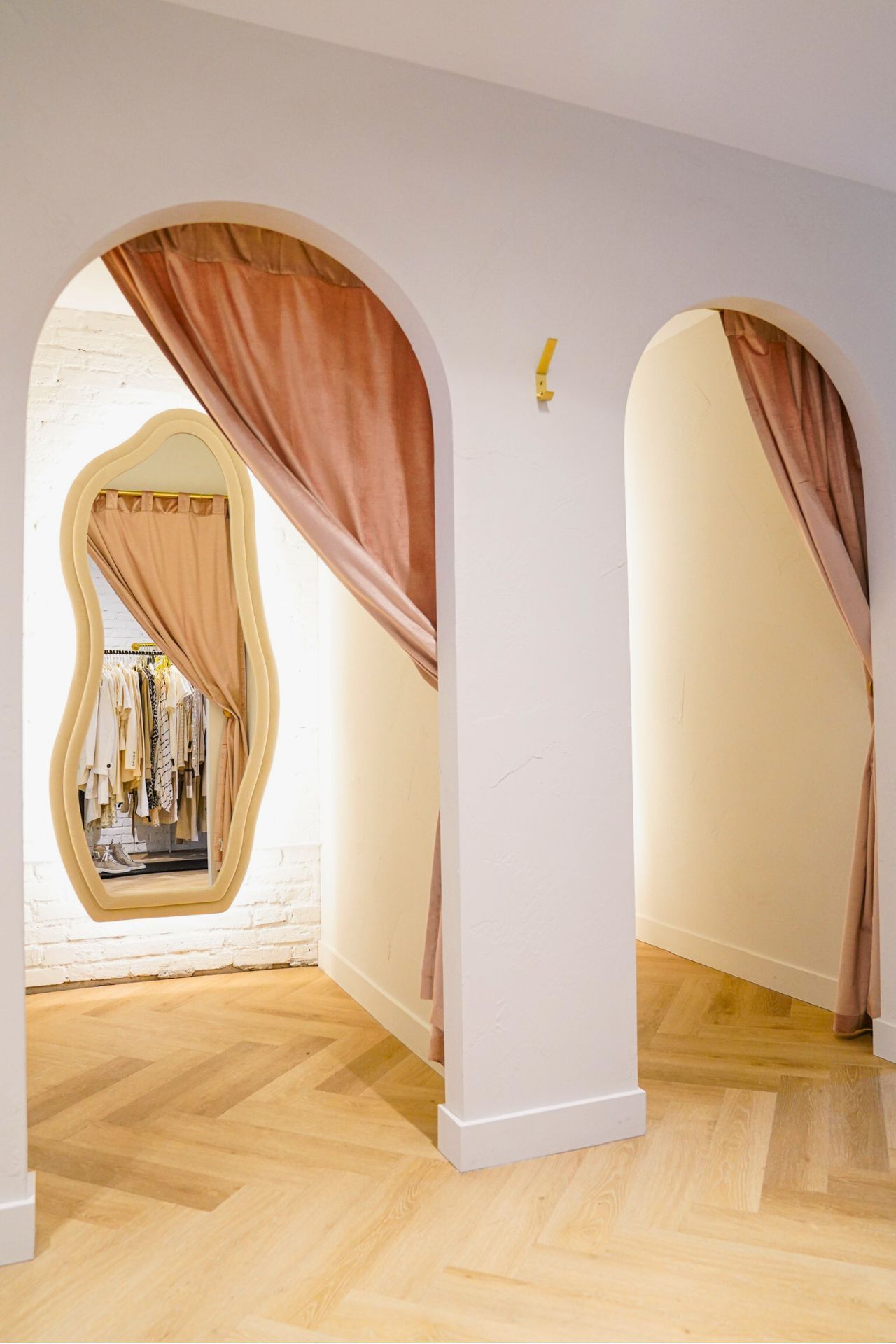 Fitting rooms with arched doorways, pink curtains, and a large mirror. Light wood floors.