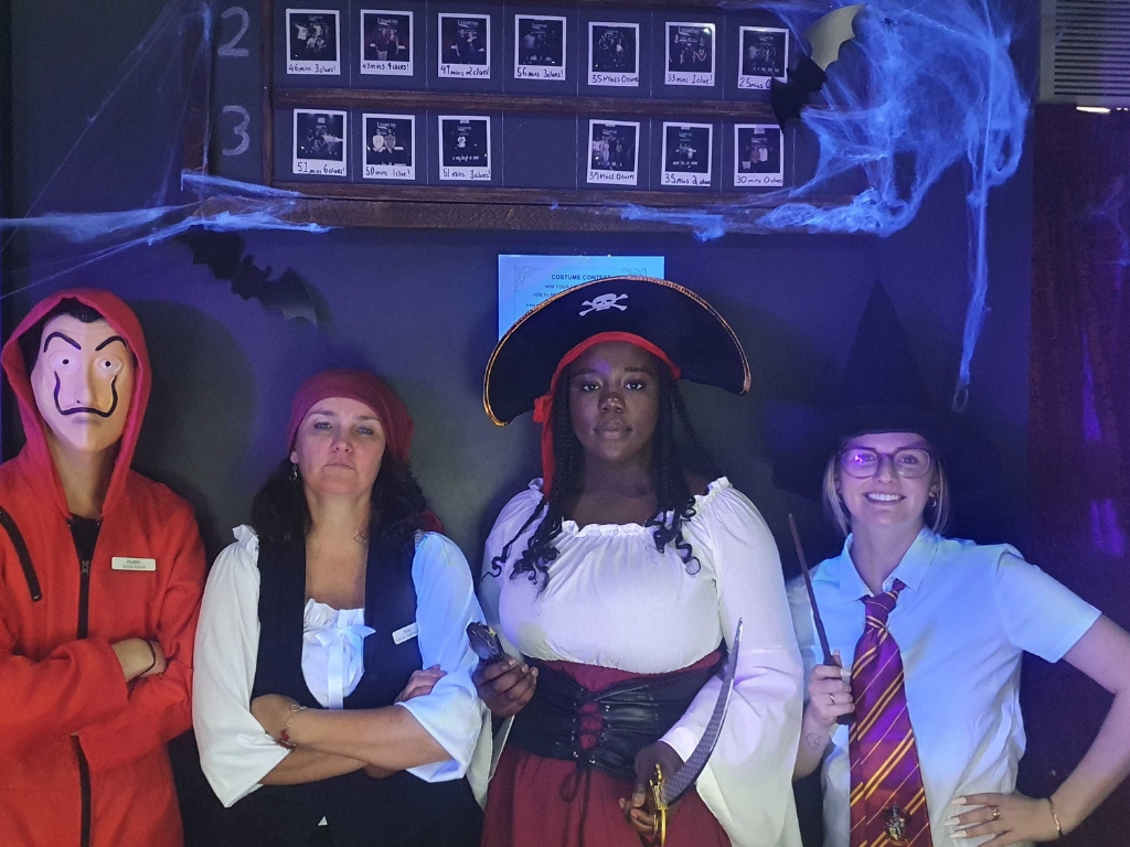 A group of escape room players dressed in Halloween costumes are posing for a picture.
