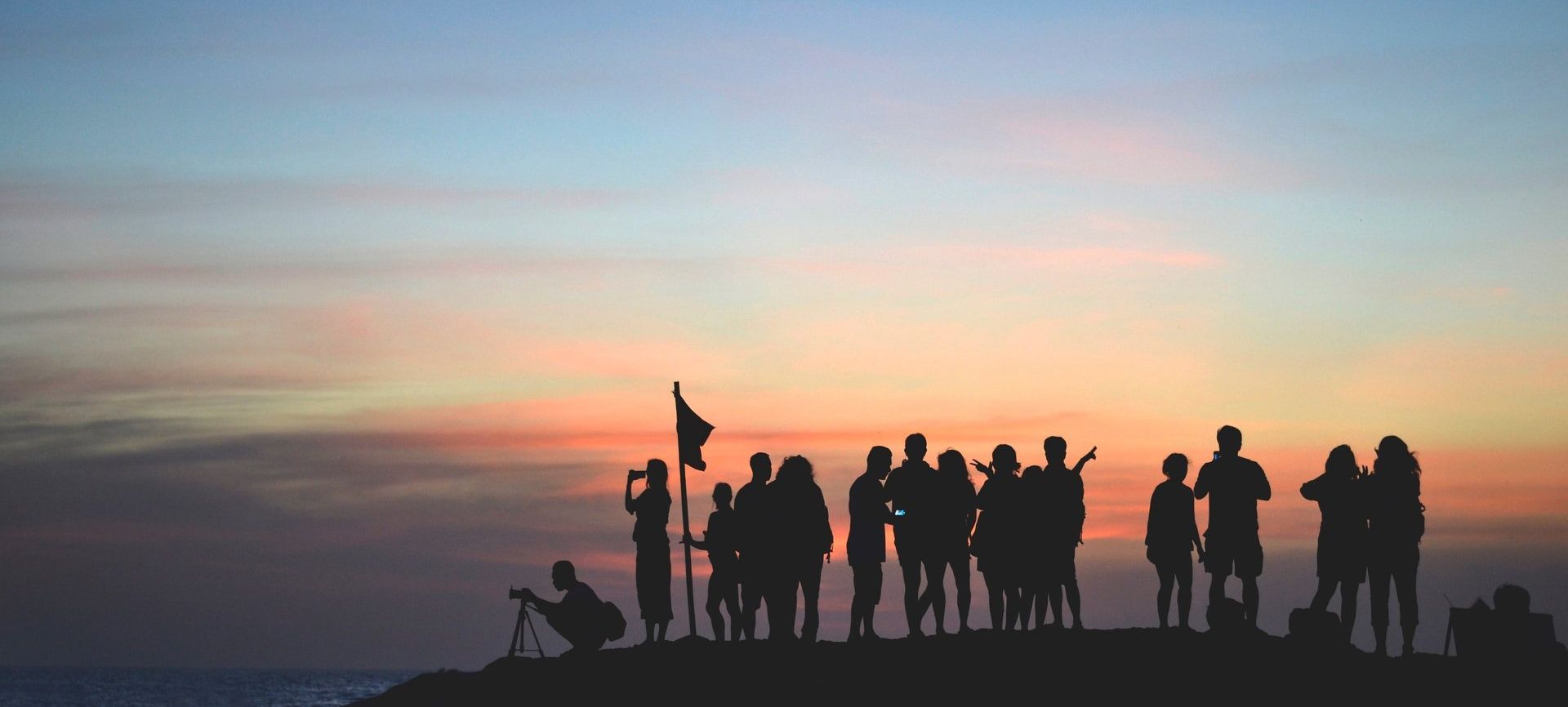 A group of people are standing on top of a hill at sunset.