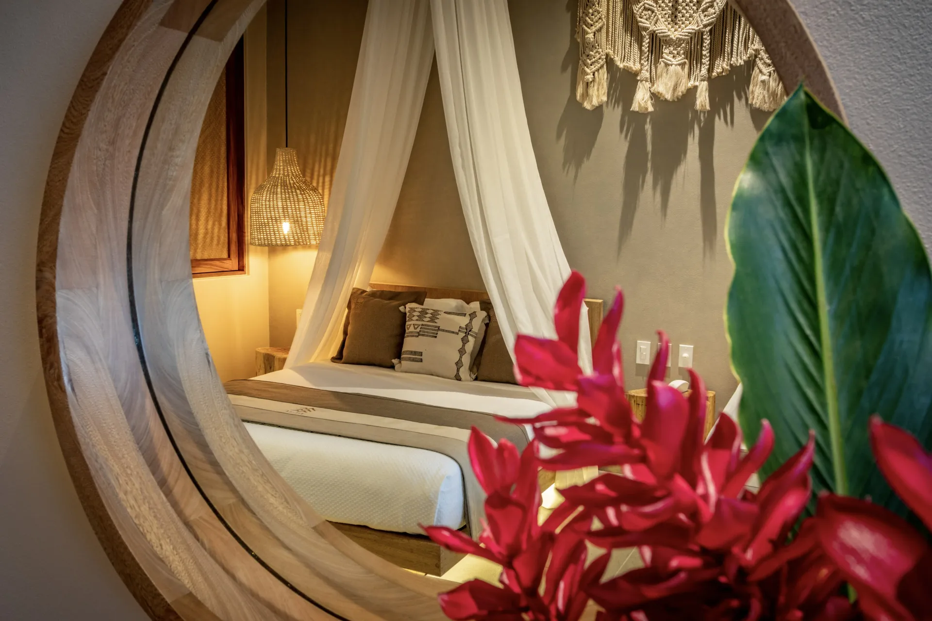 Dormitorio con cama con dosel reflejado en un espejo circular, flores rojas en primer plano.