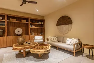 Salón con muebles de madera, estanterías, mesas y un sofá. Tonos neutros, alfombra texturizada, arte decorativo en pared