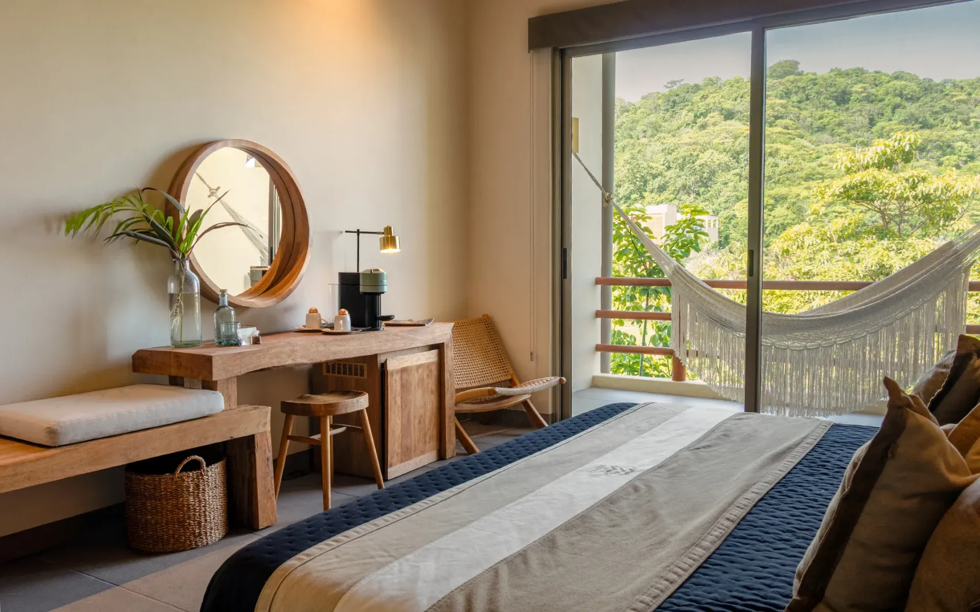 Dormitorio con cama king size, escritorio de madera y balcón con hamaca con vistas a un bosque verde.