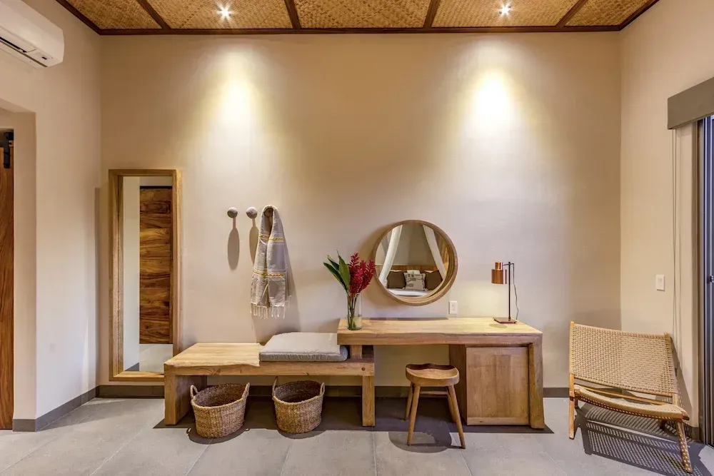 Banco de madera, escritorio, espejo y silla en una habitación con paredes de color claro y techo de mimbre.