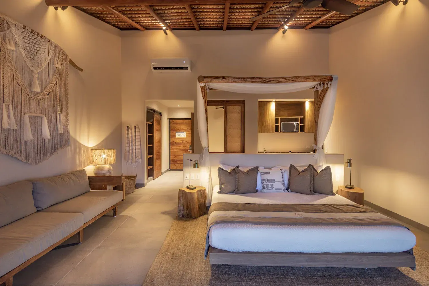 Dormitorio con cama, asientos, tapiz de macramé y detalles de madera.