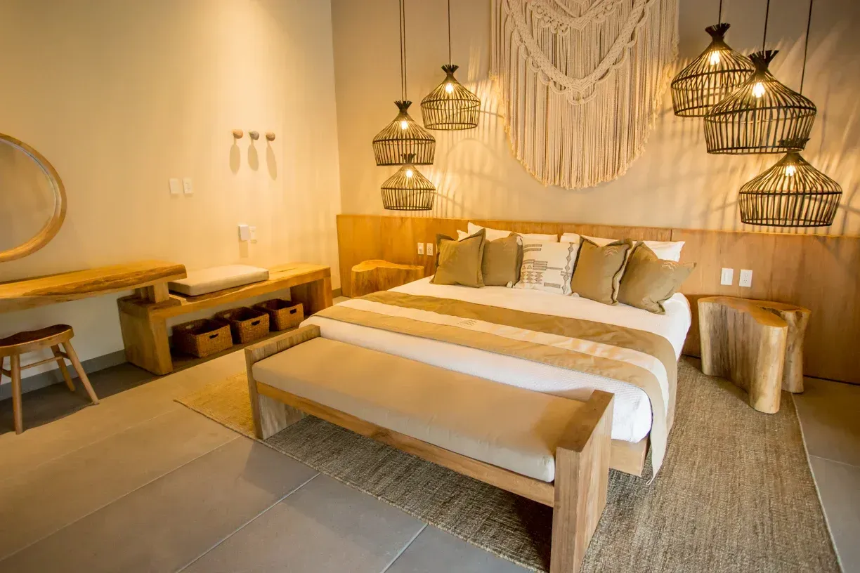 Dormitorio con cama de madera, lámparas colgantes de mimbre, tapiz de macramé, tonos neutros.