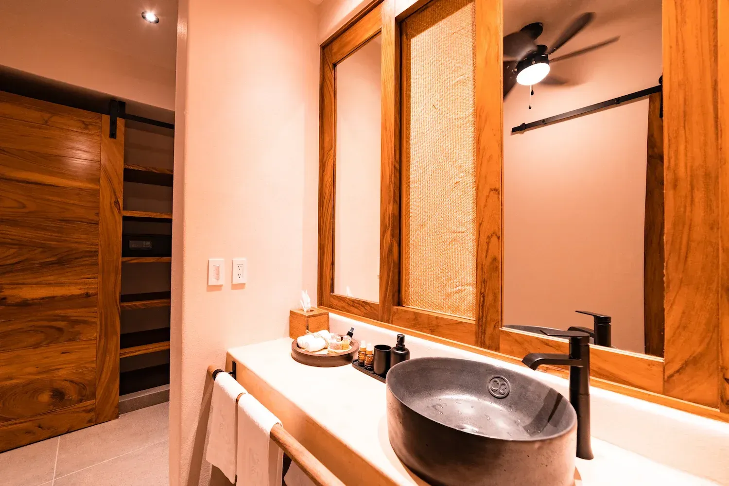 Baño con detalles de madera. Lavabo sobre encimera, espejos grandes, puerta corredera y tonos neutros.