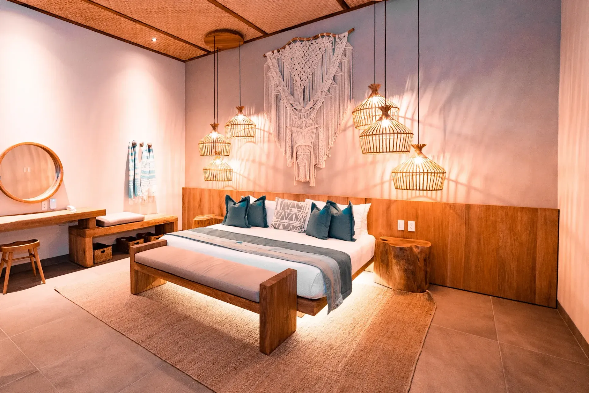 Dormitorio con detalles de madera, cama grande, macramé decorativo y lámparas colgantes.