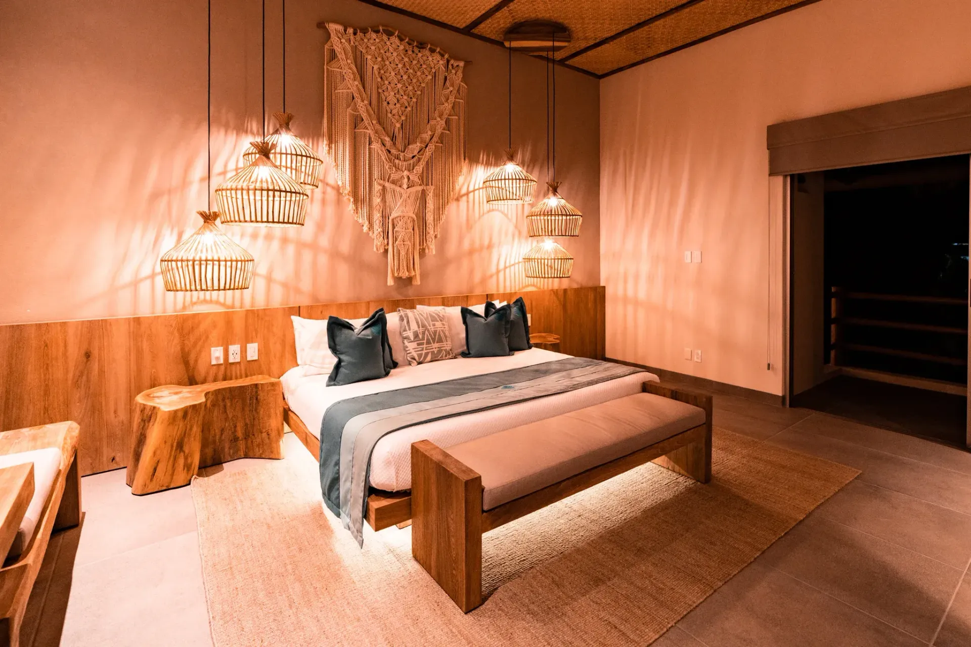 Dormitorio con cabecero de madera, tapiz de macramé y luz ambiental.