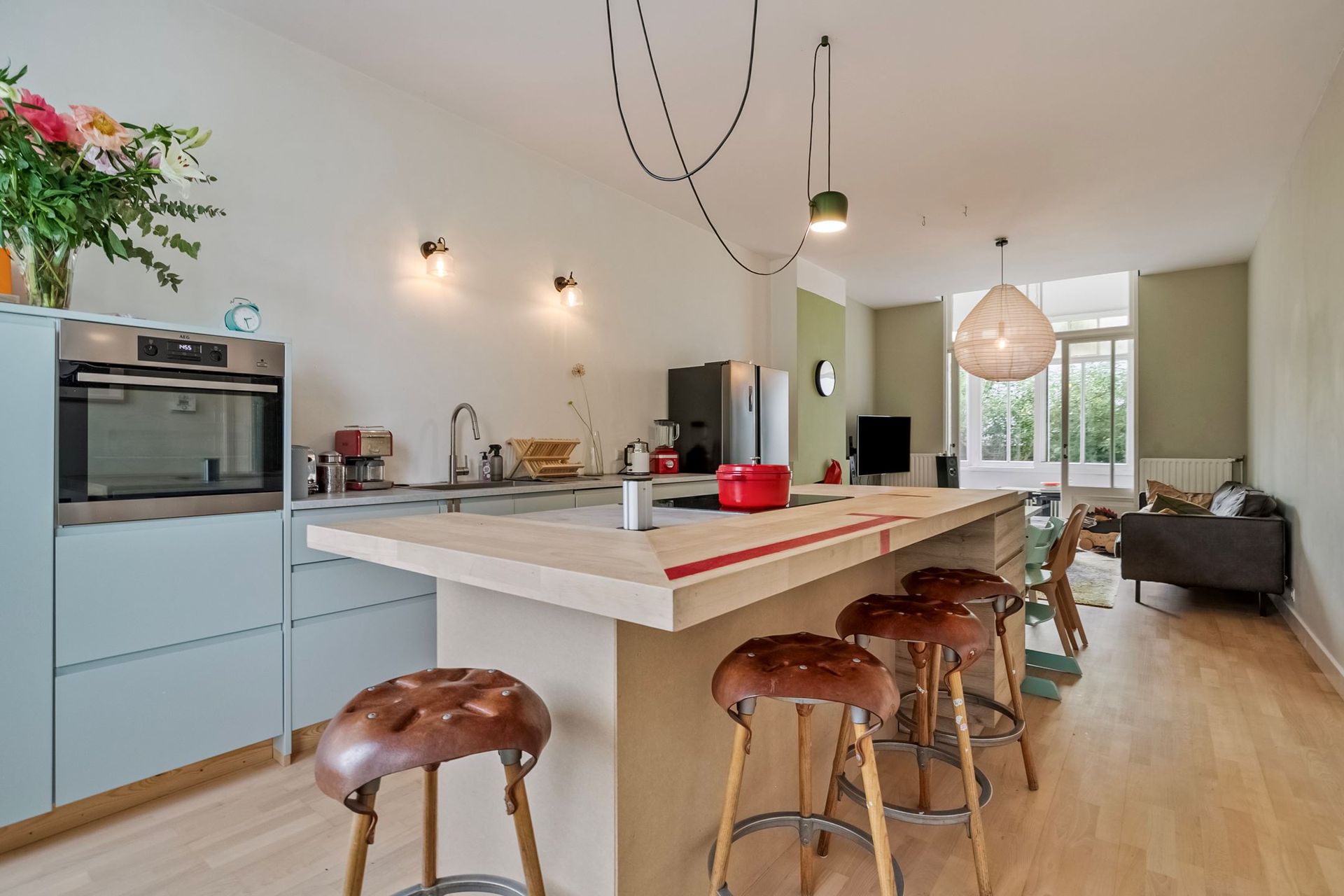 Keukeneiland met barkrukken; roestvrijstalen koelkast, rode pan; plafondlampen.