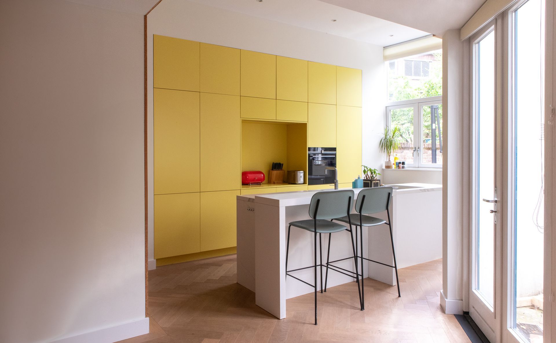 Moderne keuken met gele kastjes, een wit kookeiland en twee barkrukken.