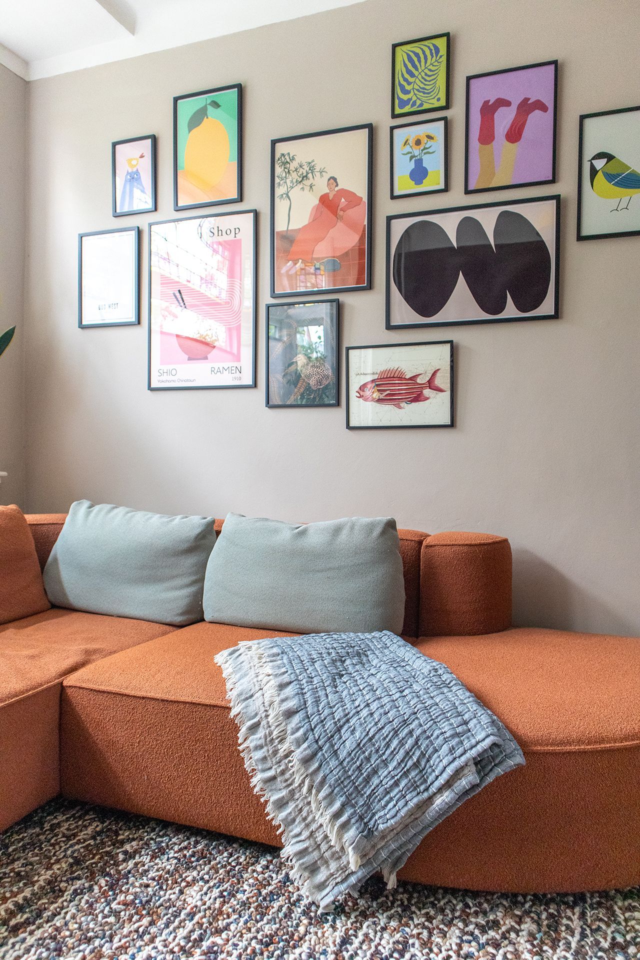 Een woonkamer gezien door een deuropening: oranje bank, vloerkleed met patroon, kleurrijk glas-in-lood, potplanten en natuurlijk licht.