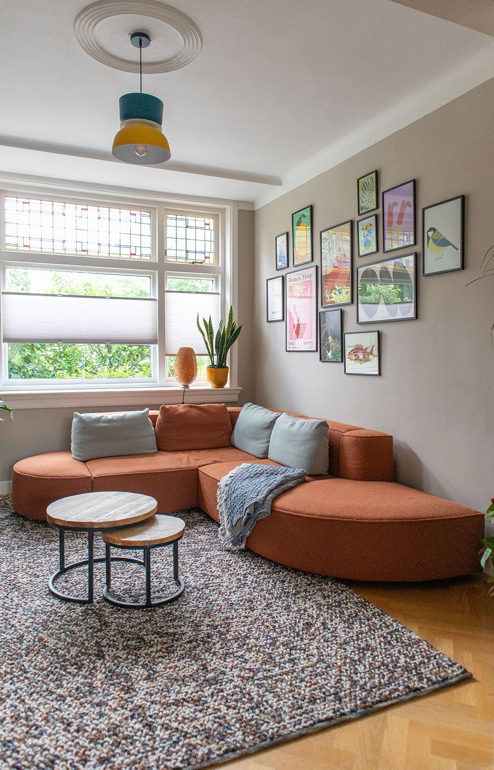 Woonkamer met roestkleurige hoekbank, fotowand en vloerkleed met patroon.