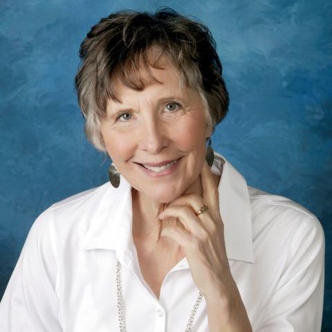 A woman in a white shirt is smiling with her hand on her chin