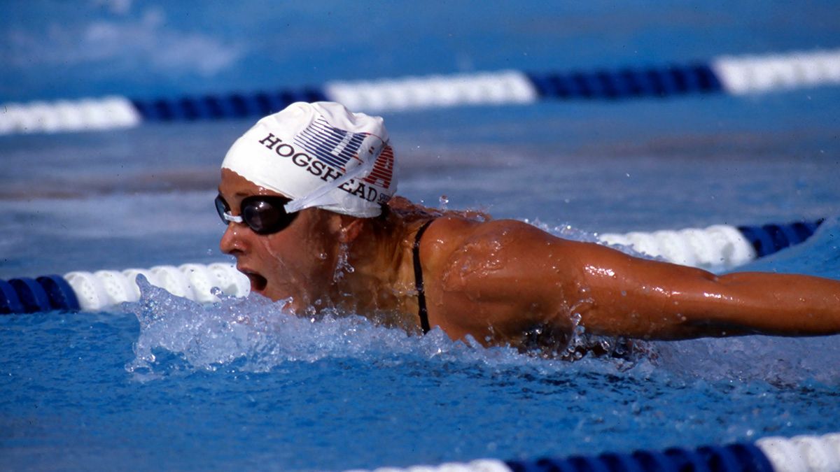 A woman is swimming in a pool wearing a rossfit hat