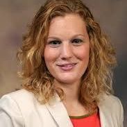 A woman with curly hair is wearing a white jacket and a red shirt.