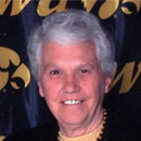 A woman with gray hair is smiling in front of a sign.