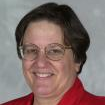 A woman wearing glasses and a red jacket is smiling for the camera.