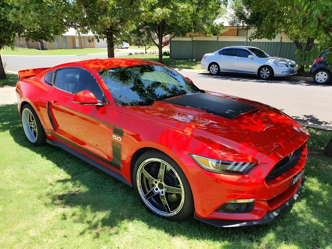 A Red Mustang is Parked in the Grass Next to a White Car — M & D Shipp Smash Repairs In Dubbo, NSW