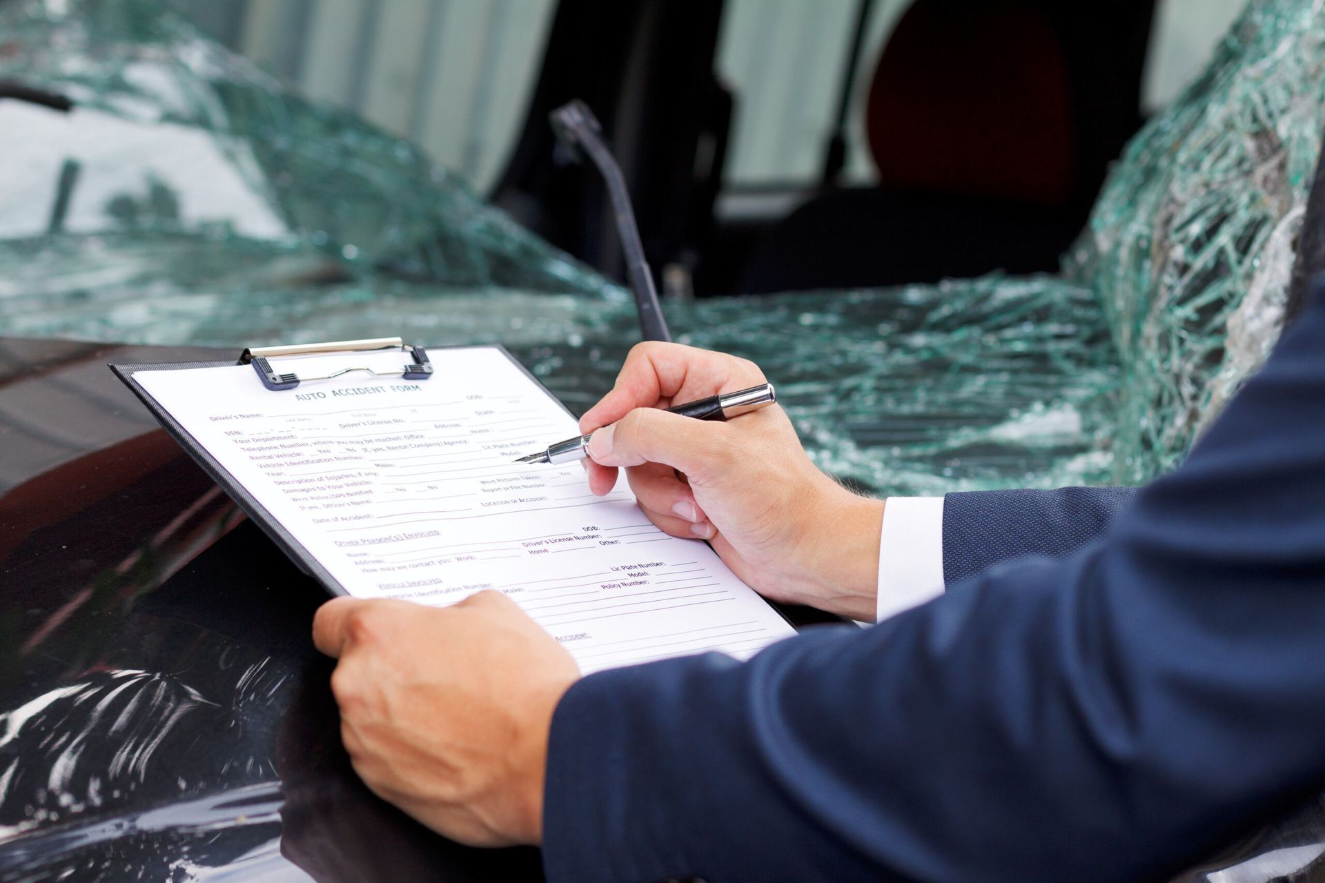 A Man is Writing on a Clipboard in Front of a Damaged Car — M & D Shipp Smash Repairs In Dubbo, NSW
