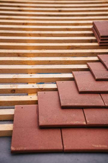 Red roof tiles being laid on wooden slats, construction.