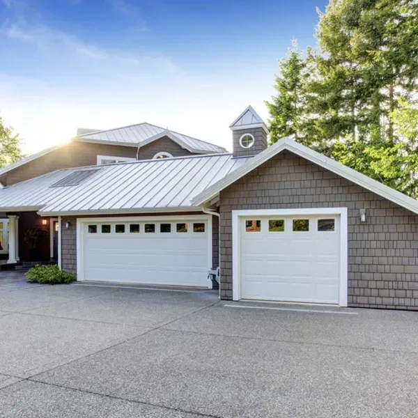 Two-car garage with white doors and gray siding, set in a driveway, sunlight.