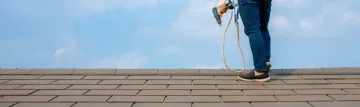 Person on a roof with safety equipment against a blue sky.