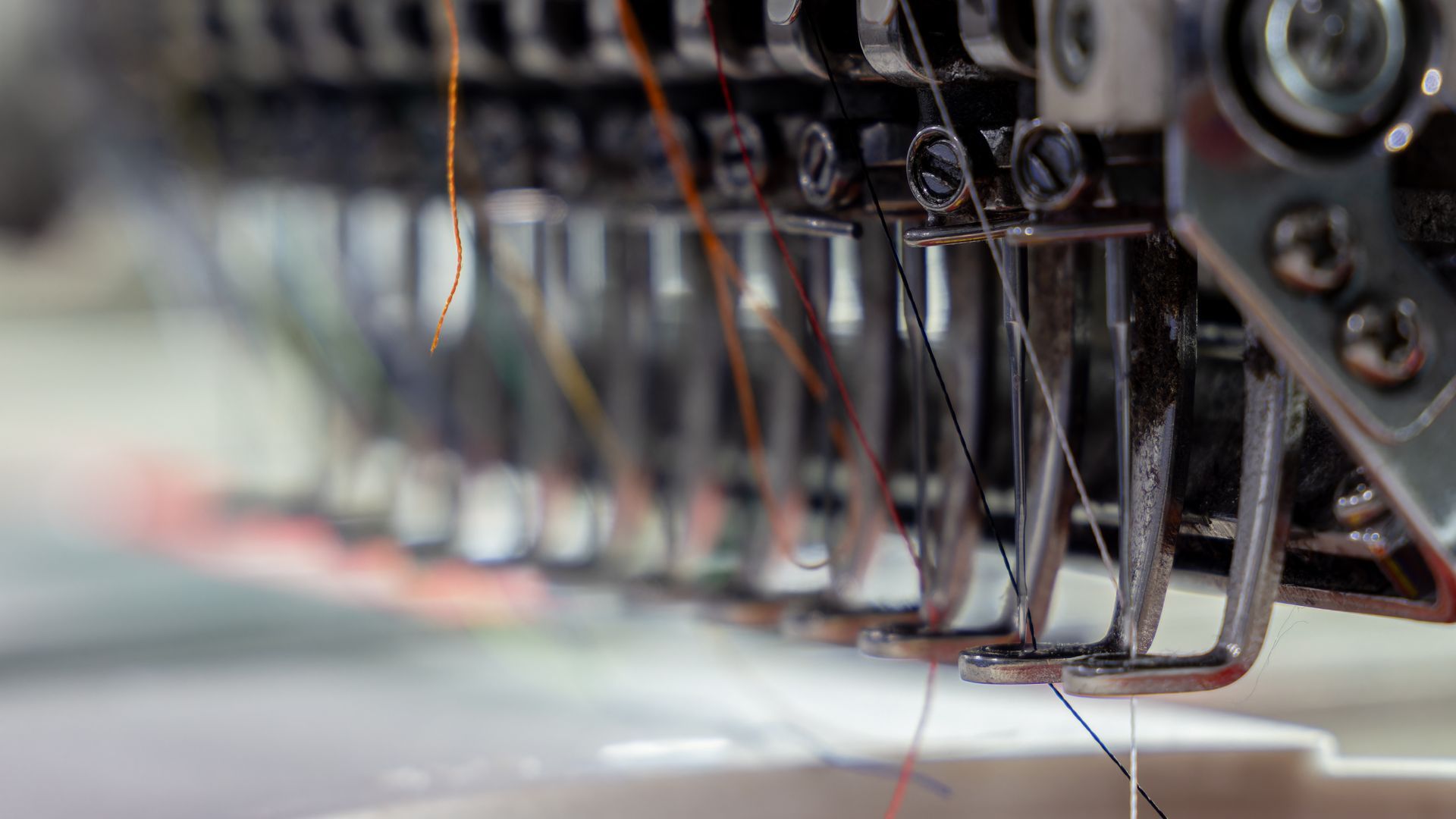Close-up of a row of industrial sewing machine needles stitching fabric on a production line