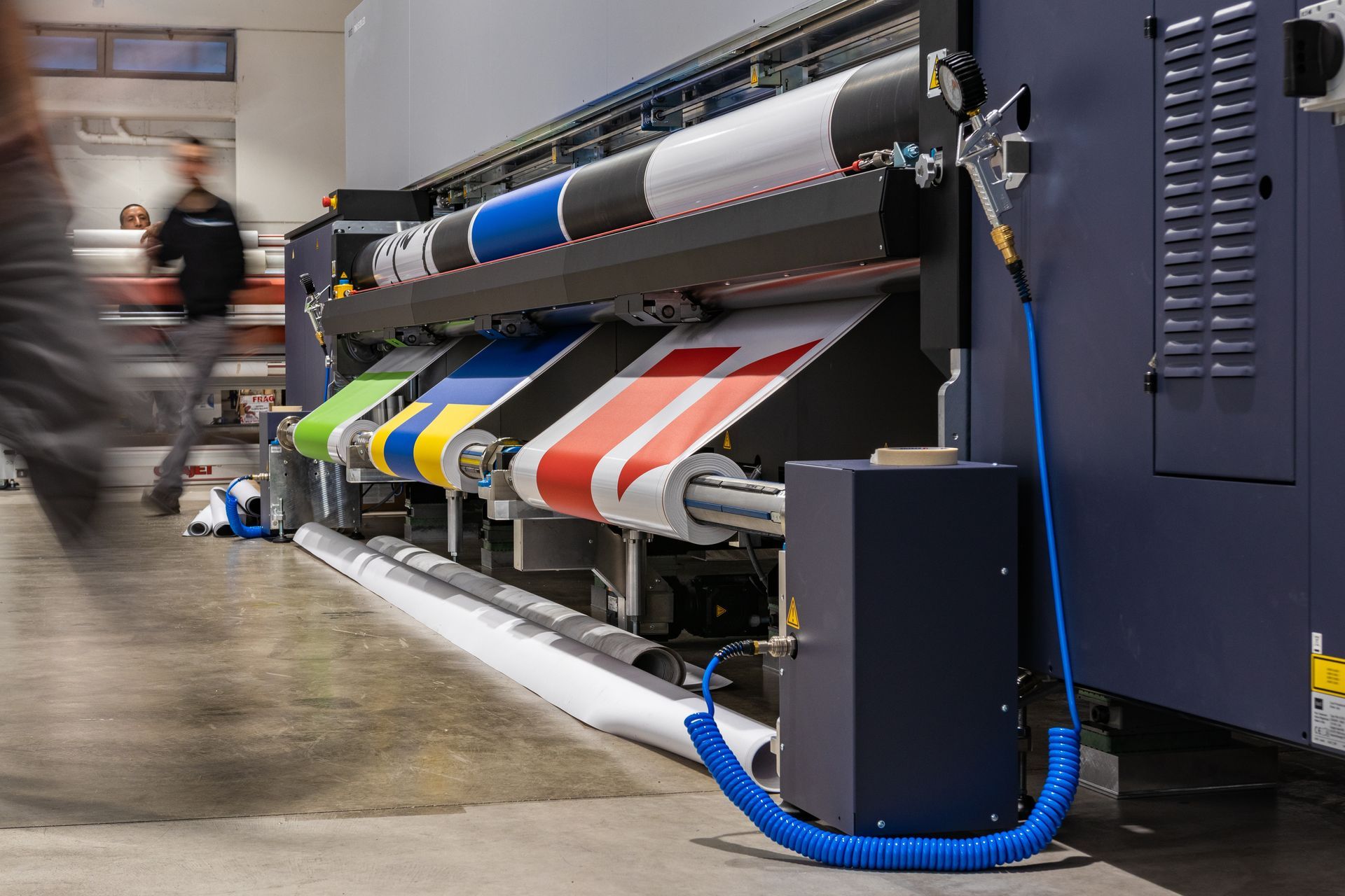 Large industrial printer printing colorful banners in a workshop, with a blurred worker beside it
